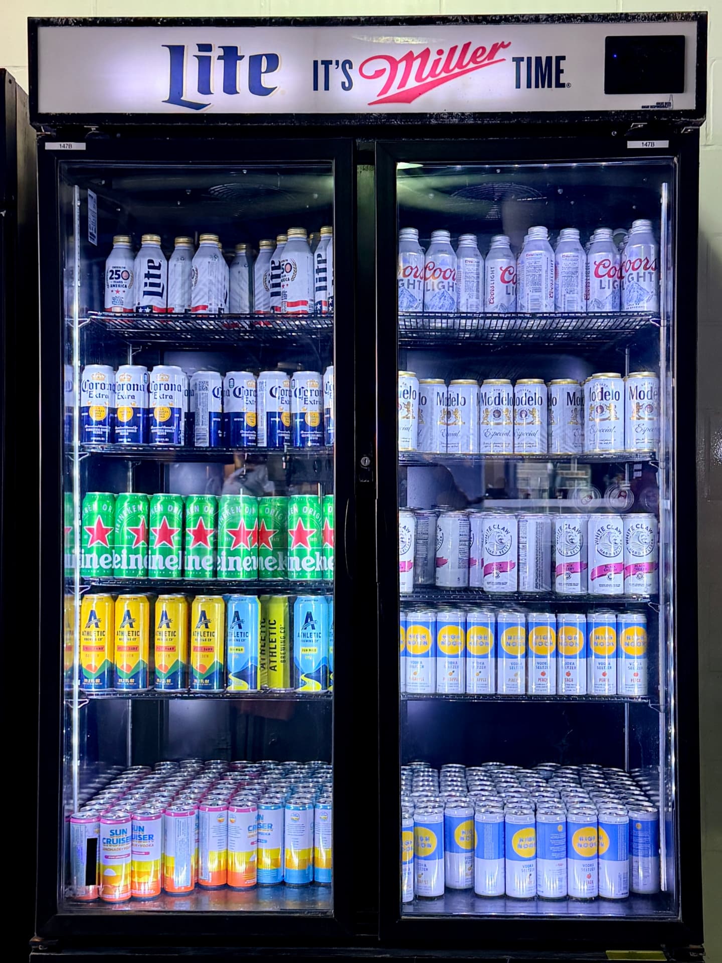 Athletic Brewing cans on one shelf beneath prominent Miller Lite signage at MetLife Stadium.